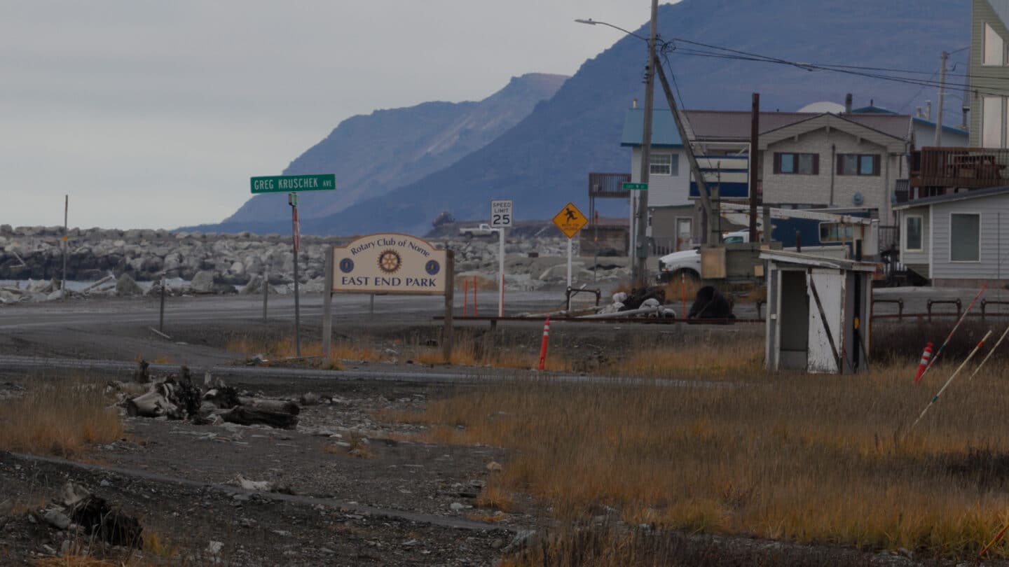 Small coastal Alaskan neighborhood near East End Park with homes, road signs, shoreline rocks, and mountains in the background