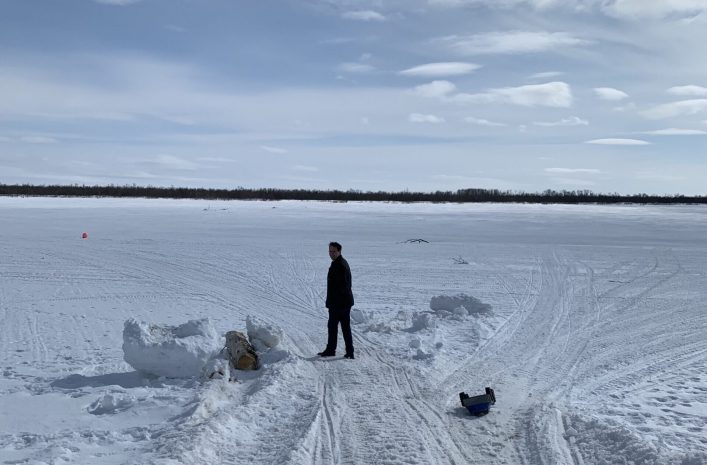 Person standing on a wide snow-covered landscape under a bright sky with distant tree line